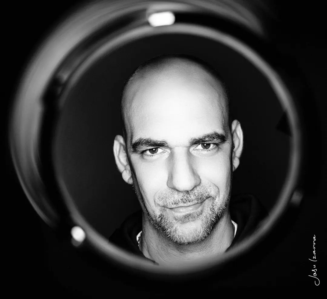 Retrato en blanco y negro de un hombre visto a través del barril de un objetivo, por Josu Izarra